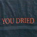 Primo piano delle lettere "YOU DRIED" ricamate in rosso